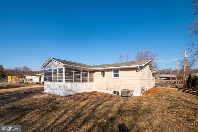 rear view of house with central AC, a lawn, and a sunroom