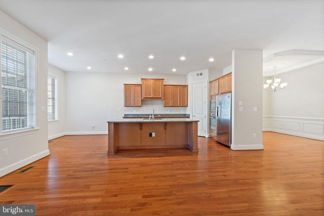 kitchen with stainless steel appliances, a center island with sink, a chandelier, and light hardwood / wood-style flooring