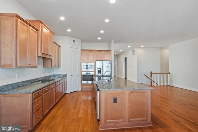 kitchen with appliances with stainless steel finishes, an island with sink, dark stone counters, and light wood-type flooring