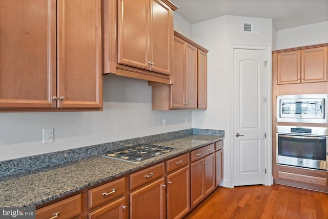 kitchen with light hardwood / wood-style flooring, dark stone counters, and appliances with stainless steel finishes