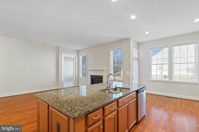 kitchen featuring sink, a center island with sink, light hardwood / wood-style flooring, dishwasher, and dark stone counters