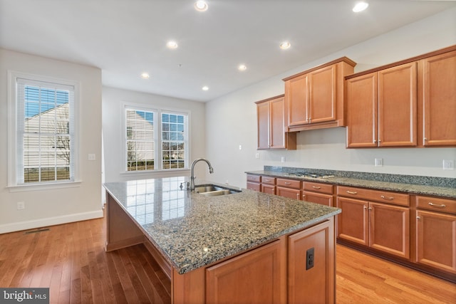 kitchen with sink, light hardwood / wood-style floors, stone counters, and a center island with sink