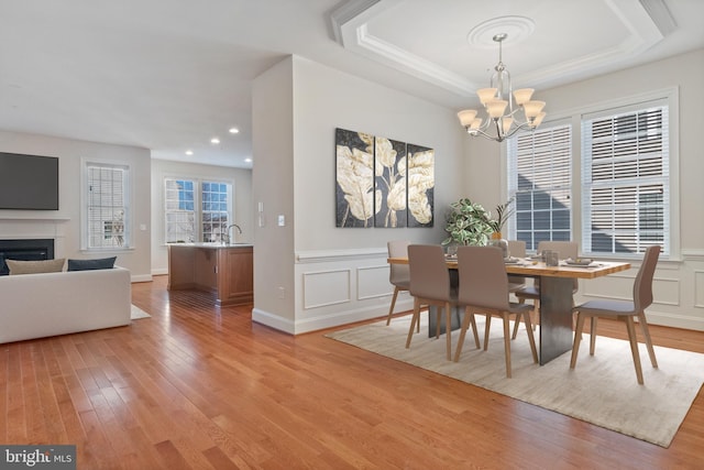 dining space featuring an inviting chandelier, sink, a raised ceiling, and light wood-type flooring