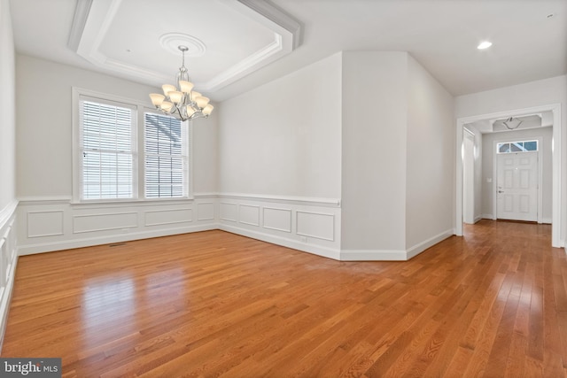 unfurnished room featuring a notable chandelier, a tray ceiling, and light hardwood / wood-style floors