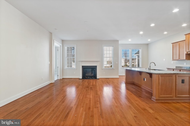 kitchen with sink, a breakfast bar area, light stone counters, light hardwood / wood-style flooring, and an island with sink