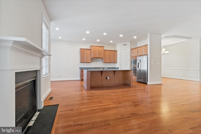 kitchen featuring a breakfast bar, light wood-type flooring, stainless steel appliances, a center island with sink, and an inviting chandelier