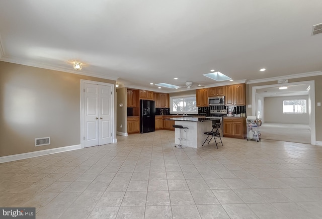 kitchen featuring a center island, crown molding, a skylight, stainless steel appliances, and a breakfast bar area