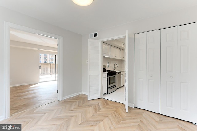 kitchen with sink, white cabinetry, light parquet floors, and stainless steel range oven