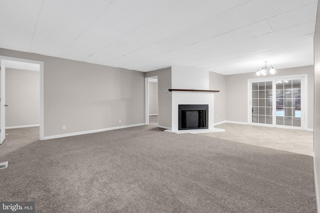 unfurnished living room with a chandelier, carpet floors, and a brick fireplace