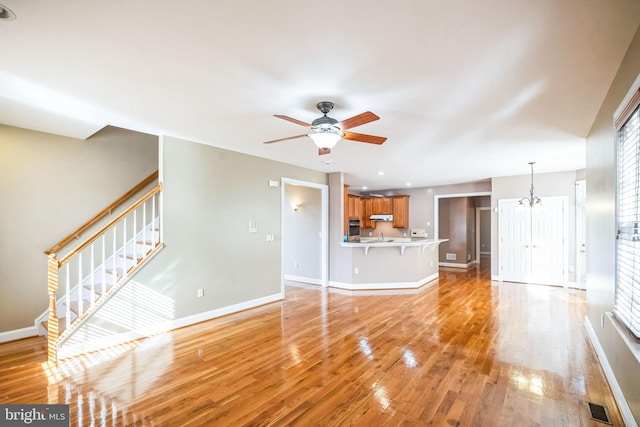 unfurnished living room featuring sink, ceiling fan with notable chandelier, a wealth of natural light, and light wood-type flooring