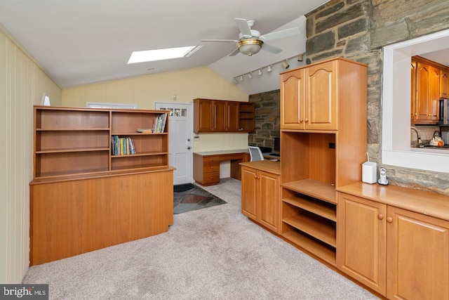 kitchen featuring ceiling fan, vaulted ceiling with skylight, light colored carpet, and built in desk