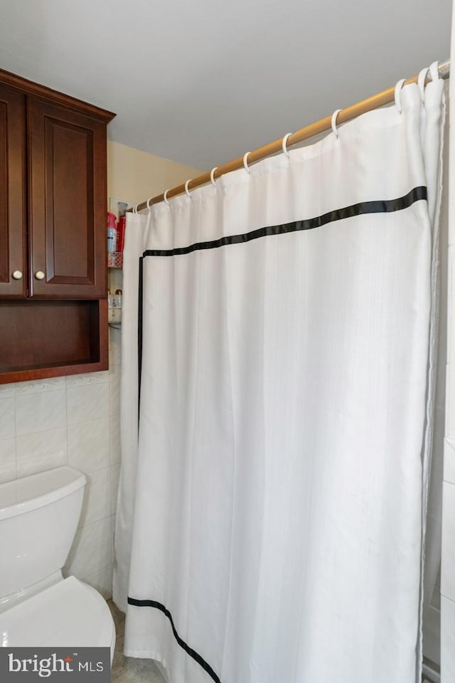 bathroom featuring toilet and tile walls