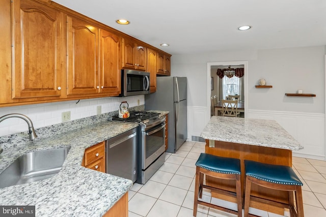 kitchen featuring a breakfast bar area, stainless steel appliances, light tile patterned flooring, light stone countertops, and sink