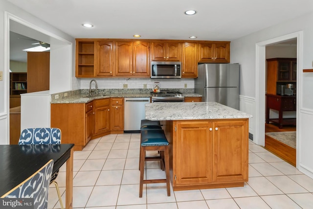 kitchen featuring appliances with stainless steel finishes, backsplash, a center island, light stone countertops, and sink