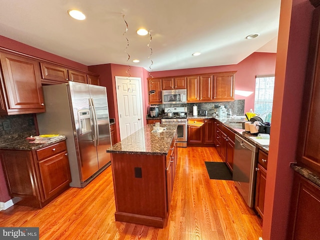 kitchen with a kitchen island, appliances with stainless steel finishes, light wood-type flooring, tasteful backsplash, and dark stone countertops