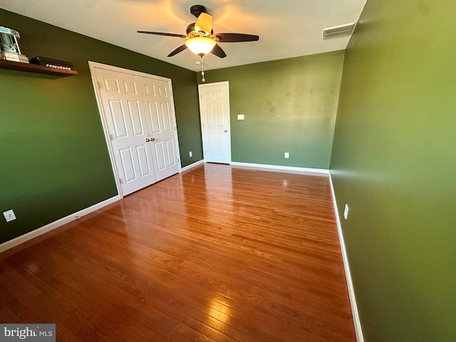 unfurnished bedroom with a ceiling fan, wood finished floors, visible vents, and baseboards