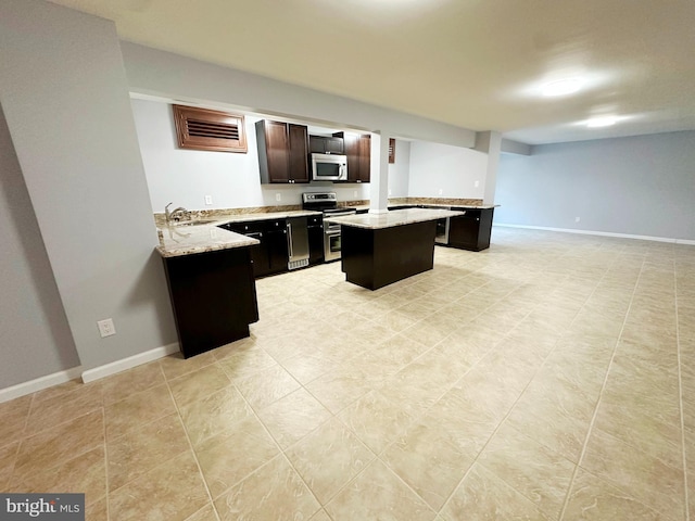 kitchen with baseboards, a kitchen island, appliances with stainless steel finishes, light stone countertops, and a sink