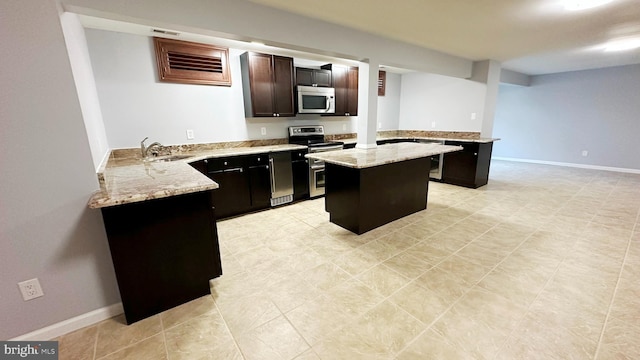 kitchen with a peninsula, a sink, a kitchen island, appliances with stainless steel finishes, and light stone countertops