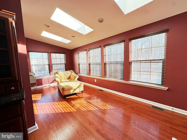 living area featuring vaulted ceiling with skylight, visible vents, baseboards, and wood finished floors