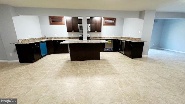 kitchen with light stone counters, stainless steel appliances, a peninsula, dark brown cabinets, and a center island