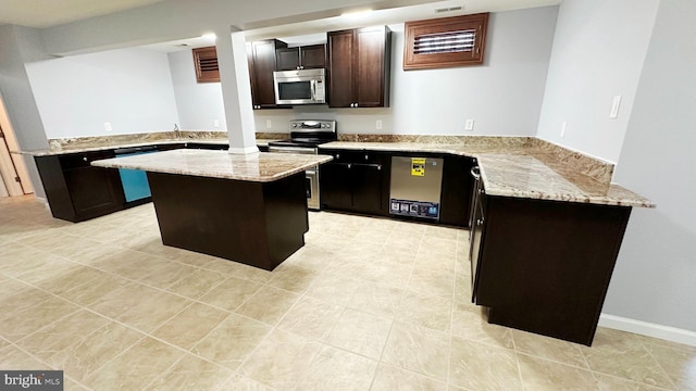 kitchen with appliances with stainless steel finishes, a kitchen island, dark brown cabinets, light stone countertops, and a peninsula