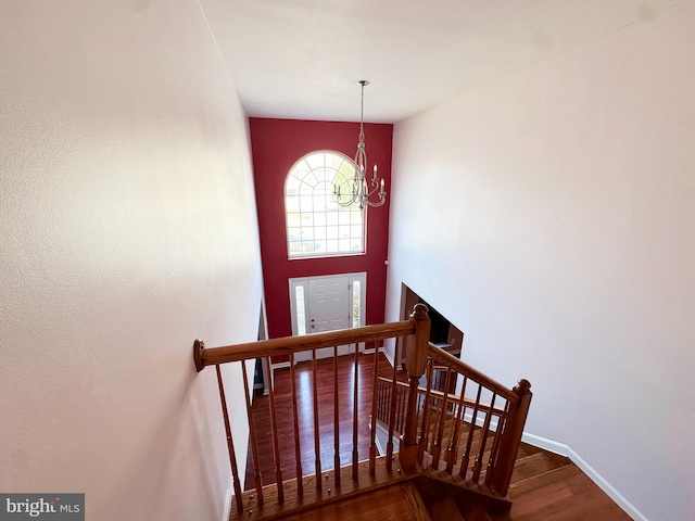 stairway featuring baseboards, a high ceiling, a chandelier, and wood finished floors