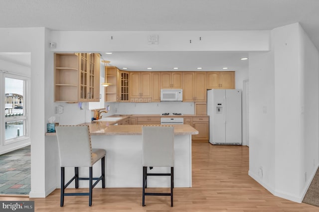 kitchen featuring white appliances, light brown cabinetry, sink, kitchen peninsula, and a breakfast bar area