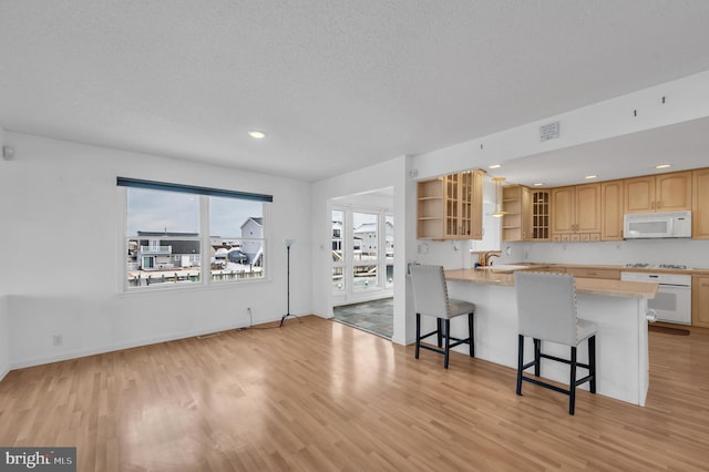 kitchen featuring light hardwood / wood-style floors, white appliances, kitchen peninsula, and a breakfast bar area