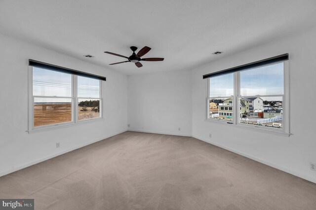 unfurnished room with ceiling fan, light colored carpet, and plenty of natural light