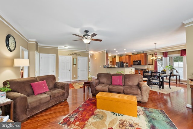 living room with light wood-type flooring, ceiling fan with notable chandelier, and crown molding