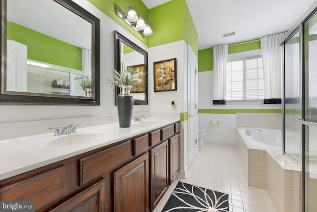 bathroom featuring tile patterned flooring, vanity, tiled bath, and toilet