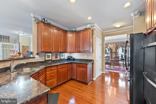 kitchen with an inviting chandelier, black refrigerator, sink, ornamental molding, and light wood-type flooring