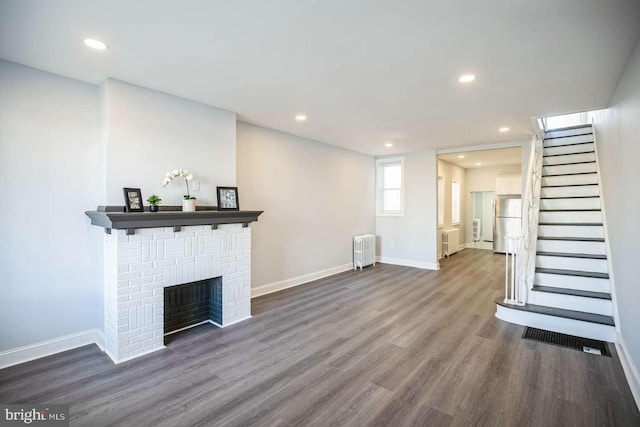 unfurnished living room featuring radiator heating unit, a brick fireplace, and dark wood-type flooring