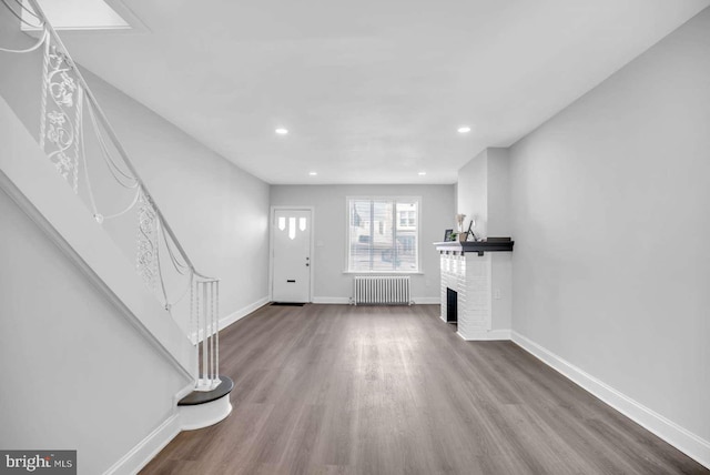 interior space featuring hardwood / wood-style flooring, radiator heating unit, and a brick fireplace