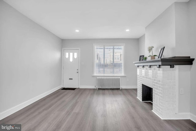 unfurnished living room featuring a fireplace, radiator, and light hardwood / wood-style flooring