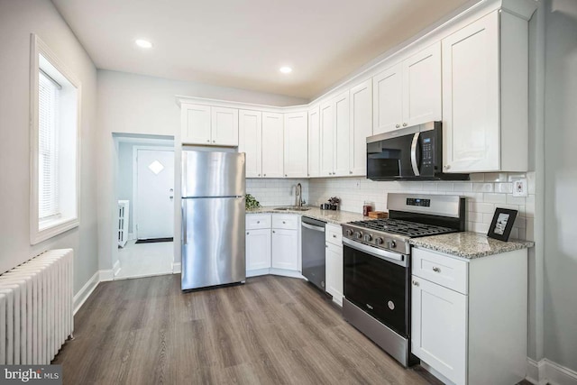 kitchen featuring radiator, sink, light hardwood / wood-style floors, white cabinetry, and stainless steel appliances