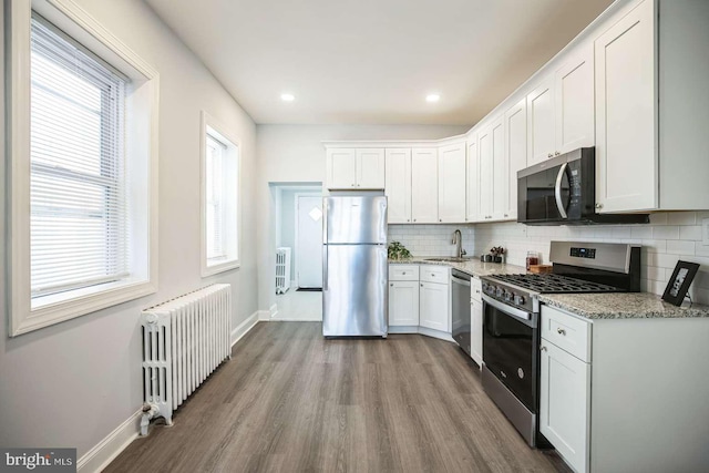 kitchen with white cabinets, decorative backsplash, radiator heating unit, and appliances with stainless steel finishes