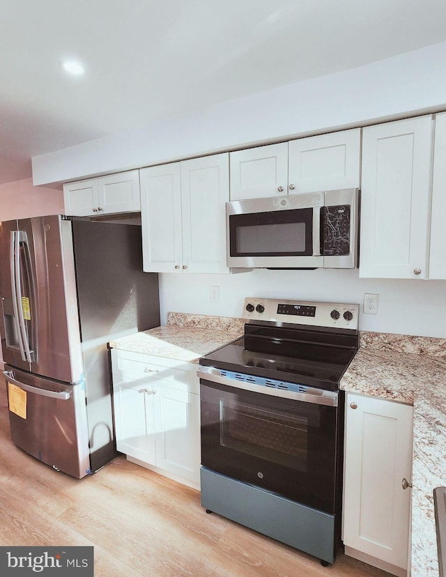 kitchen with white cabinetry, appliances with stainless steel finishes, light stone counters, and light hardwood / wood-style flooring