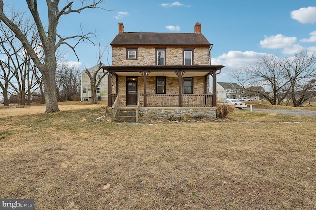 view of front of house featuring covered porch, stone siding, a chimney, and a front yard