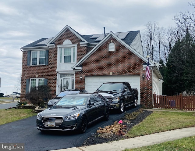 traditional home featuring a garage, aphalt driveway, fence, roof mounted solar panels, and brick siding