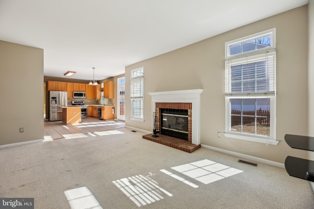 unfurnished living room with light colored carpet, a fireplace, visible vents, and baseboards