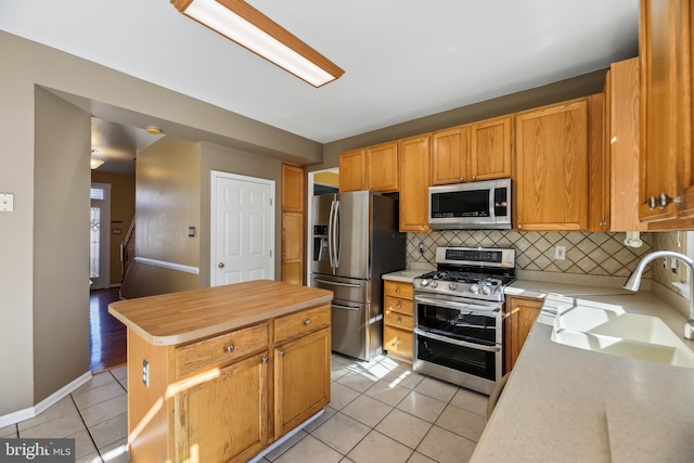 kitchen with decorative backsplash, appliances with stainless steel finishes, light countertops, a sink, and light tile patterned flooring