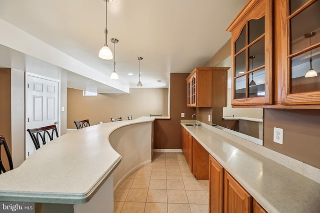 kitchen with brown cabinetry, light tile patterned floors, light countertops, and a sink