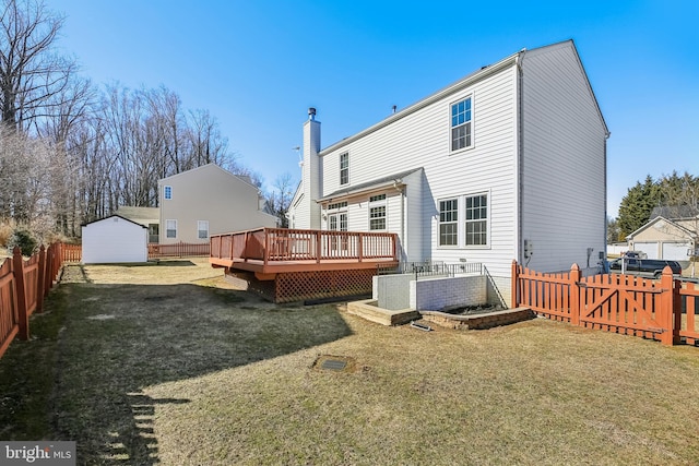 back of property with a deck, an outbuilding, a fenced backyard, a lawn, and a chimney