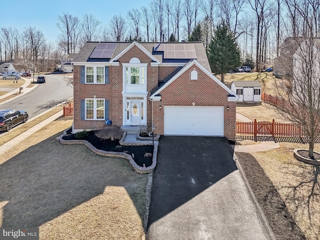 view of front of house with driveway, brick siding, solar panels, and fence