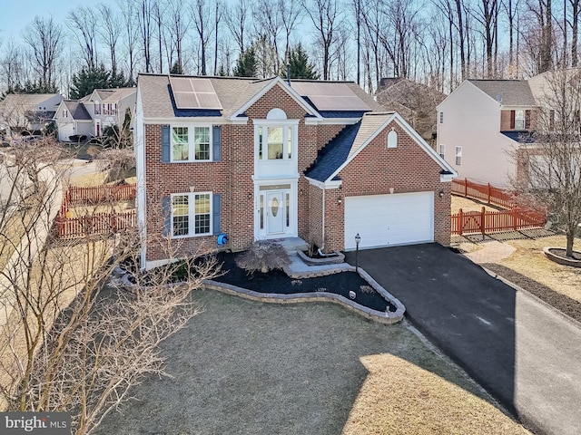 view of front facade featuring brick siding, driveway, an attached garage, and fence