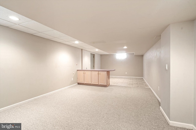 basement featuring a drop ceiling, light colored carpet, and bar