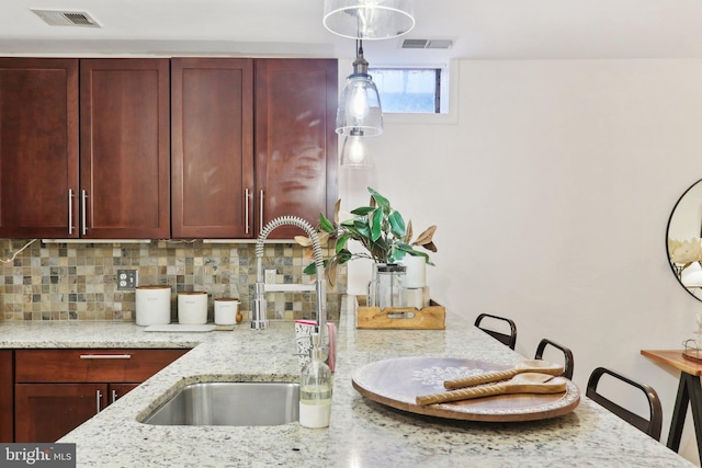 kitchen featuring sink, backsplash, light stone counters, and decorative light fixtures