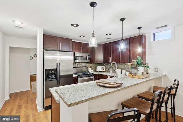 kitchen featuring a breakfast bar, stainless steel appliances, light stone counters, decorative light fixtures, and kitchen peninsula