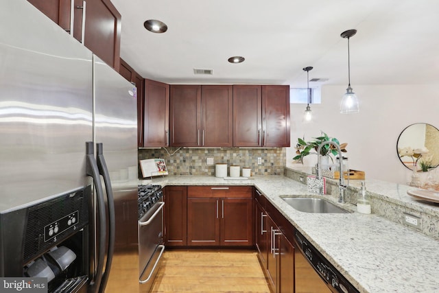 kitchen with sink, light stone counters, hanging light fixtures, appliances with stainless steel finishes, and kitchen peninsula